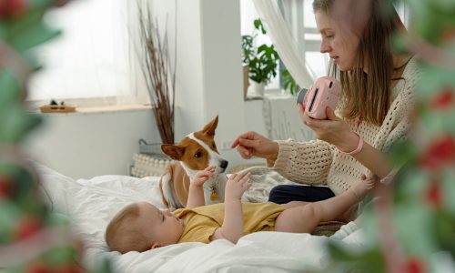 mom plays with baby and dog on bed at home