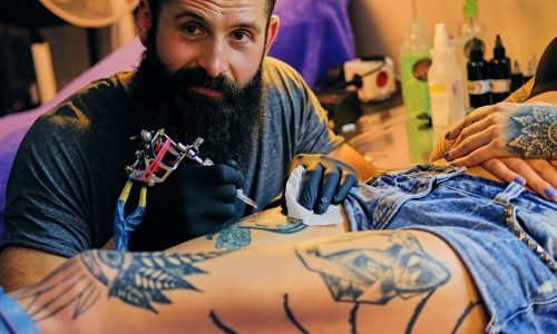 Tattoo male artist makes a tattoo on a female leg.
